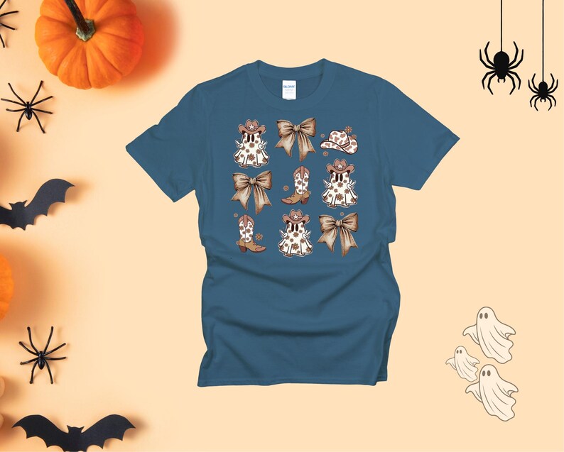May include: A teal t-shirt featuring a repeating pattern of cartoon ghosts wearing cowboy hats and boots, with brown bows. The design has a Halloween theme. The shirt is a short-sleeved crew neck.