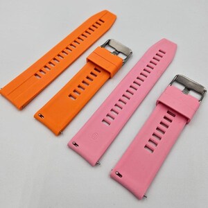 Two silicone watch straps in bright orange and light pink (baby pink) colors, unisex replacement bands with stainless steel buckles and quick release system.