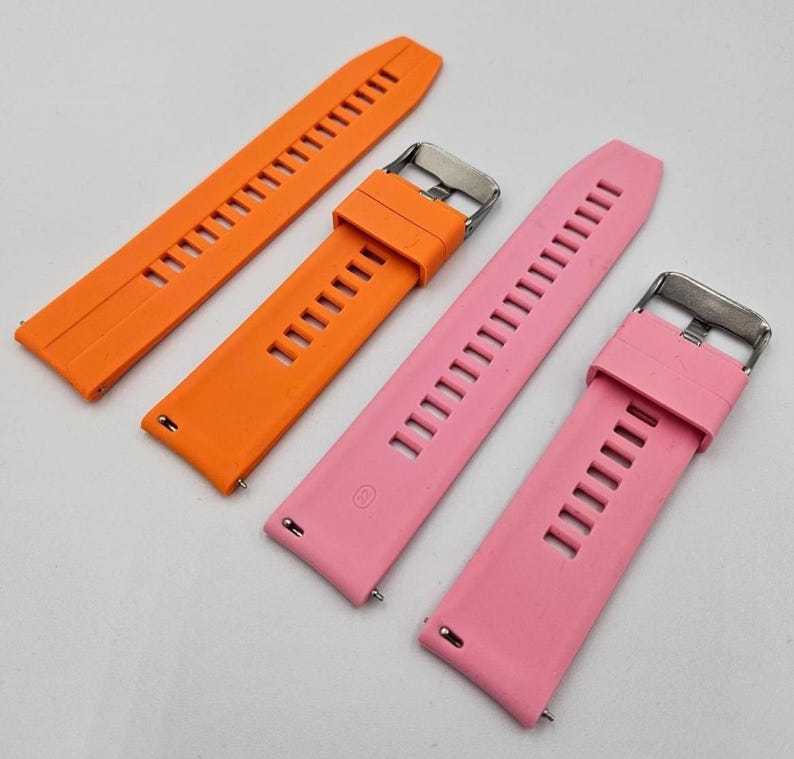 Two silicone watch straps in bright orange and light pink (baby pink) colors, unisex replacement bands with stainless steel buckles and quick release system.