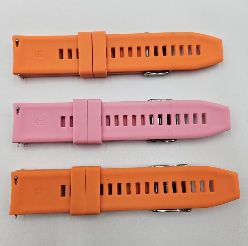 Two silicone watch straps in bright orange and light pink (baby pink) colors, unisex replacement bands with stainless steel buckles and quick release system.