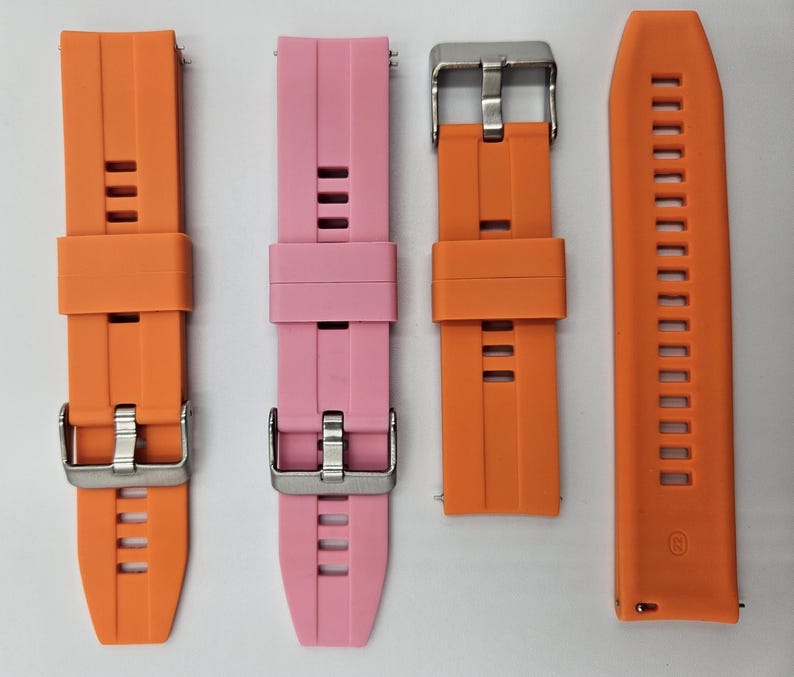 Two silicone watch straps in bright orange and light pink (baby pink) colors, unisex replacement bands with stainless steel buckles and quick release system.