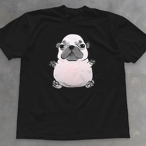 Pode incluir: Camiseta preta com uma ilustração de desenho animado de um buldogue francês. O buldogue é branco e cinza, com uma cabeça grande e orelhas pequenas. A camiseta é feita de um material macio. A ilustração do buldogue é centralizada.