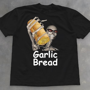 Könnte beinhalten: Schwarzes T-Shirt mit einem Skelett mit Sonnenbrille, das ein Brot mit Knoblauch hält. Die Worte "Garlic Bread" sind weiß gedruckt. Das T-Shirt ist aus einem weichen Material.