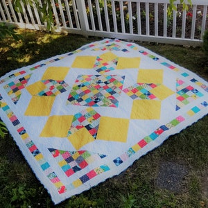 May include: A patchwork quilt with a yellow and white geometric design. The quilt is made with a variety of colourful fabrics and has a blue and white border.