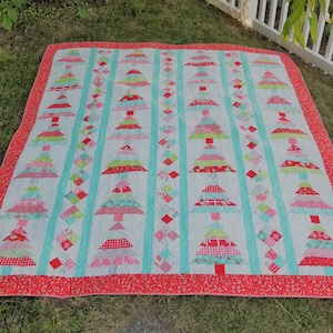 Pode incluir: Um edredom branco com uma borda vermelha e um padrão de árvores de Natal coloridas. As árvores são feitas de diferentes tecidos e cores, incluindo vermelho, verde, rosa e azul.