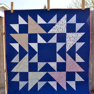May include: A blue quilt with a star pattern made from various fabrics with red, white, and blue colors. The quilt is hanging on a clothesline.