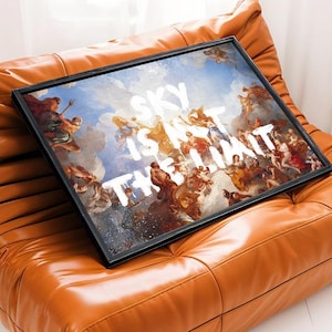 Könnte beinhalten: Ein gerahmter Kunstdruck mit einem klassischen Gemälde von Figuren vor blauem Himmel. Der weiße Text lautet "SKY IS NOT THE LIMIT". Der Druck liegt auf einem braunen Ledersofa.