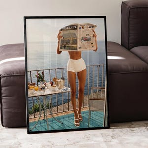 Può includere: Stampa incorniciata con una persona in pantaloncini bianchi e sandali che legge un giornale con il titolo "Dolce Vita" su un balcone con vista sul mare. È visibile un tavolo con articoli per la colazione.