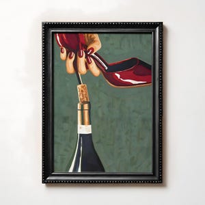 Puede incluir: Una impresión artística enmarcada representa una botella de vino con un corcho que está siendo retirado por un zapato de tacón alto rojo. La obra de arte presenta un fondo verde oscuro y un marco negro. El zapato y la mano están pintados de forma realista.