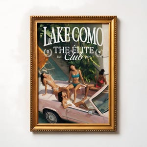 May include: A framed print with a vintage illustration of women in swimwear on a pink convertible. The print reads "Lake Como The Elite Club" in white, set within a gold-coloured frame.