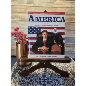 May include: A hardcover book titled "AMERICA" with the text "A Citizen's Guide to Democracy Inaction" and "With a Foreword by Thomas Jefferson." The cover features a man, an eagle, and the American flag.