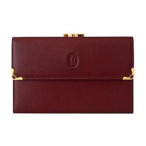 May include: A rectangular burgundy leather wallet with a textured finish. The front features a centered embossed circular logo and gold-tone metal corner accents on the flap. A gold-tone metal clasp is visible at the top edge of the wallet.