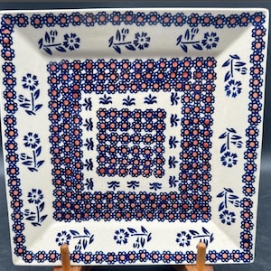 May include: A white ceramic square serving dish with a blue and pink floral pattern. The dish has a raised rim and a decorative border.