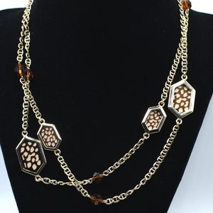 May include: A gold chain necklace with brown and white patterned octagon-shaped pendants. The necklace has brown crystal accents.