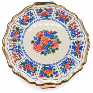 May include: A round, scalloped-edge compact mirror featuring a cream-colored enamel surface with a central floral bouquet and a border of eight smaller floral clusters in vibrant shades of orange, blue, and green, finished with a gold-tone metal rim.
