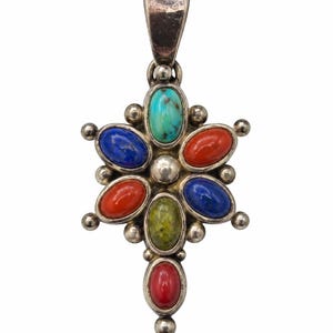 May include: A silver pendant featuring a central cluster of seven oval-shaped cabochon gemstones in turquoise, red, blue, and green. The stones are arranged in a flower-like pattern with small silver spheres between each stone and a large bail at the top.