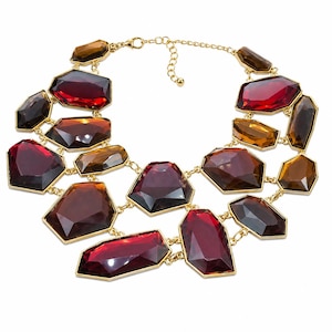 May include: A statement necklace featuring multiple faceted, geometric-shaped resin stones in deep shades of red, burgundy, and amber. The stones are set in gold-toned metal frames and connected by gold-toned metal links, forming a layered collar.