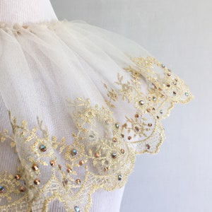May include: A white tulle collar with a gold lace trim and iridescent rhinestones.