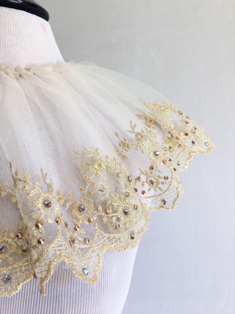 May include: A white tulle collar with a gold lace trim and iridescent rhinestones.