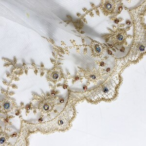May include: Gold lace trim with iridescent beads and a scalloped edge. The lace is on a white background.