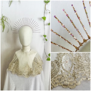 May include: A white lace bridal cape with a delicate gold trim. The cape is worn over a white mannequin with a pink and silver halo headband. The halo headband is made of wire and has small, iridescent beads.
