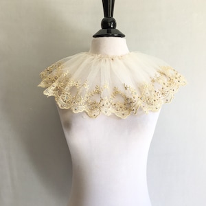 May include: A white tulle collar with gold embroidery and rhinestones. The collar is on a white mannequin.