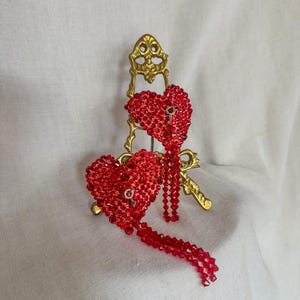 May include: Two red heart-shaped earrings with crystal embellishments and dangling crystal strands.