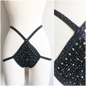 Puede incluir: Lingerie negra con un diseño de tirantes cruzados y un panel frontal en forma de triángulo cubierto de pedrería iridiscente.