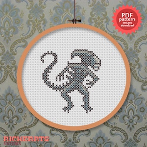 May include: Cross stitch pattern of a grey alien in a white embroidery hoop. The pattern is available as an instant PDF download.