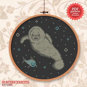 May include: Cross-stitch pattern of a manatee and a small fish in a dark blue background, framed in a wooden hoop. The manatee is gray, and the fish is blue. The text "PDF pattern instant download" is in a red starburst.