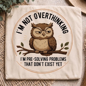 Könnte beinhalten: Ein cremefarbenes T-Shirt mit einer kreisförmigen Grafik einer braunen Eule auf einem Ast. Der Text I'M NOT OVERTHINKING und I'M PRE-SOLVING PROBLEMS THAT DON'T EXIST YET ist in schwarzen Großbuchstaben um die Eulenillustration angeordnet.