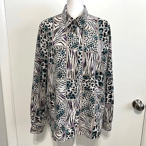 May include: A button-down shirt with a patchwork design featuring zebra stripes, leopard spots, and geometric patterns in black, white, purple, and teal. The long-sleeved shirt has a classic collar and buttoned cuffs.