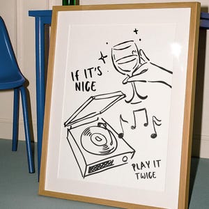 May include: A framed art print with a wooden frame. The black and white illustration features a wine glass, musical notes, and a record player. Text on the print reads "If it's nice, play it twice."