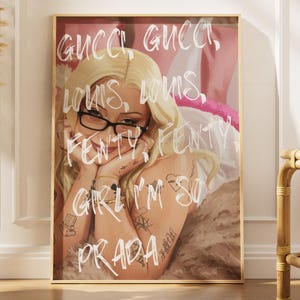 Pode incluir: Uma impressão de arte emoldurada com uma mulher loira usando óculos, com as palavras "GUCCI, LOUIS, FENTY, GIRL I'M SO PRADA" escritas em branco. A obra de arte tem um esquema de cores rosa e marrom.