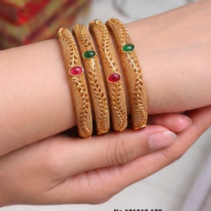 May include: Four gold-toned bangles with a textured matte finish and a leaf-like pattern. Each bangle features a single oval-shaped stone, alternating between red and green. Text on the image reads: No.401812-180, Matte Finish, Priemum Quality, Size : 2/4/6/8.