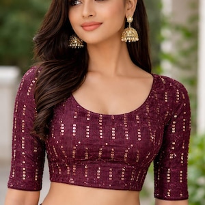 May include: A burgundy crop top and skirt set, adorned with gold sequins. The top features a scoop neck and three-quarter sleeves. Gold earrings are worn. This outfit is suitable for special occasions and events.