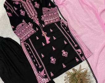 May include: A black long-sleeved tunic featuring intricate pink embroidery and mirror accents along the neckline, cuffs, and hem. The set includes matching black trousers with embroidered hems and a sheer, light pink dupatta with a black lace border.