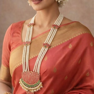 May include: A multi-strand pearl necklace featuring a large central lotus-shaped pendant with red and green enamel accents, small pearl dangles, and matching lotus-shaped stud earrings. The necklace is composed of four strands of white pearls.