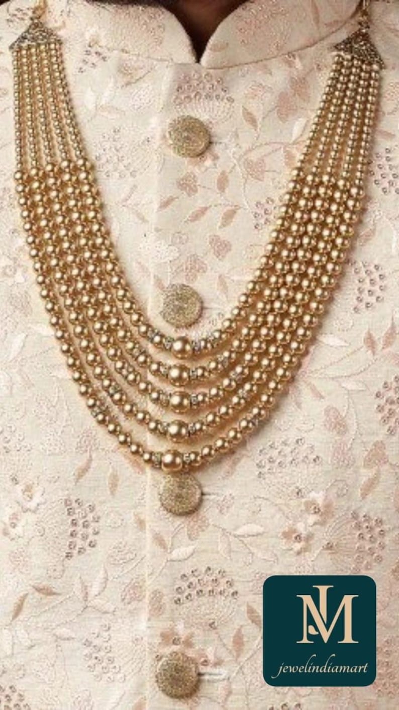 May include: A multi-strand gold-toned beaded necklace with a layered design. The necklace is worn over a cream-colored embroidered garment with gold buttons. The image includes a logo that reads "jewelindiamart".