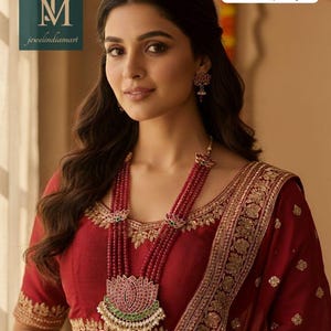 Op de afbeelding: Een vrouw draagt een lange kristallen set ketting en bijpassende oorbellen. De ketting heeft meerdere strengen rode kralen en een grote hanger met een lotusontwerp. De vrouw draagt een rode blouse met gouden borduursel.