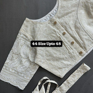 Könnte beinhalten: Cremefarbene Hakoba-Bluse aus reiner Baumwolle. Sie hat weiße Stickereien und Holzknöpfe. Die Ärmel haben ein detailliertes Paisley-Design. Der Text "44 Size Upto 48" ist sichtbar. Ein passender Gürtel ist enthalten. Traditioneller Stil.