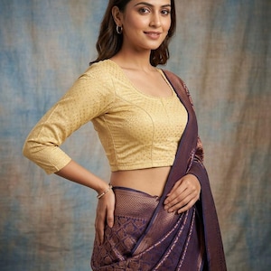 May include: A gold three-quarter sleeve blouse with a subtle textured pattern paired with a deep purple saree featuring an intricate copper-toned woven design. The blouse has a scoop neckline and the saree is draped over the shoulder with a wide border.