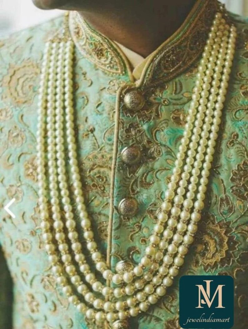 May include: A multi-strand pearl necklace with gold accents adorns a teal and gold embroidered jacket. The jacket features ornate gold detailing and large, decorative buttons. The image includes the text "jewelindiamart".