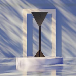 Könnte beinhalten: Eine dunkelgraue, geometrische Skulptur mit dem Text "Torus Knot" auf einer dreieckigen Spitze. Die Skulptur steht auf einem weißen Sockel vor einem blau-weißen Hintergrund. Das Design hat einen hohen, schlanken Stiel und eine dreieckige Basis.