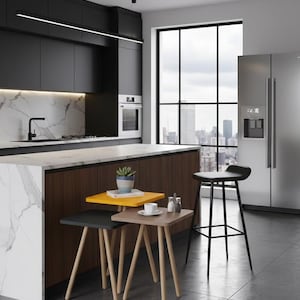 May include: A modern kitchen with a marble countertop and dark wood cabinetry. Three small square side tables in yellow, gray, and brown with light wood legs are in the foreground. A black bar stool and stainless steel refrigerator are also visible.