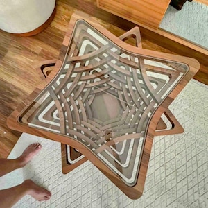 Op de afbeelding: Een stervormige houten salontafel met een glazen blad. De tafel heeft een gelaagd ontwerp met afwisselende lichte en donkere houttinten, waardoor een uniek geometrisch patroon ontstaat. De tafel heeft een diameter van ongeveer 91 cm.