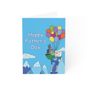 May include: A folded greeting card with a blue background and the text "Happy Father's Day." The card features a cartoon character holding balloons and a robot, with mountains and clouds in the background.