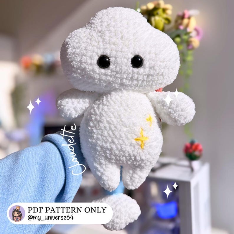 Op de afbeelding: Een witte, pluizige, wolkvormige gehaakte knuffel met zwarte ogen en een geel sterontwerp. De tekst "PDF PATTERN ONLY @my_universe64" is zichtbaar. De knuffel heeft kleine armen en benen. Het woord "Claudette" is geschreven.