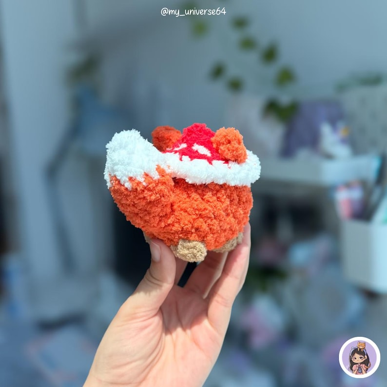 May include: A small, plush, handmade fox figurine crafted from orange and white fuzzy yarn. The fox features a prominent, bushy white-tipped tail, rounded ears, and small tan-colored feet. The text @my_universe64 is visible at the top center.