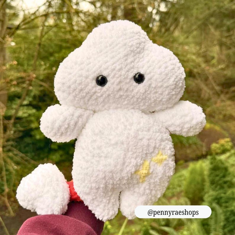Op de afbeelding: Een witte, pluche wolk-vormige knuffel met zwarte knoopogen en kleine armen en benen. Het speelgoed heeft een gele sterren design aan de zijkant. De tekst "@pennyraeshops" staat onderaan de afbeelding. Het speelgoed is zacht en pluizig.